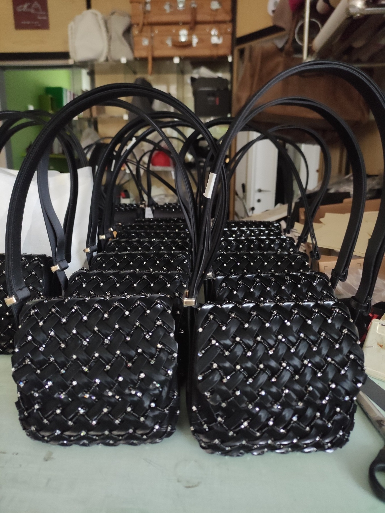 Fila di borsette nere intrecciate con cristalli, in produzione nel nostro atelier